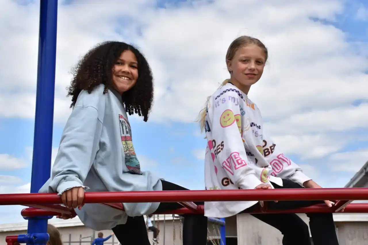 Two students smiling on the playground climbing frame under a blue sky